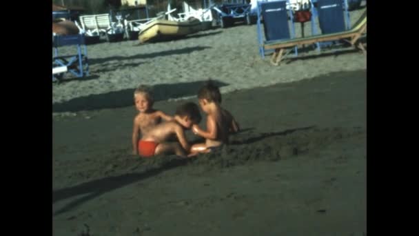 エルバ島 イタリア1971年6月 小さな子供たちがビーチの休暇のシーンで砂の上で遊ぶ 70年代の海の休暇の家族の思い出 — ストック動画