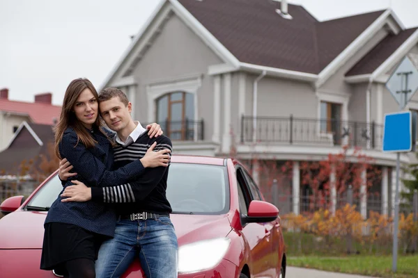Fiatal család közelében a ház háttér piros autó — Stock Fotó
