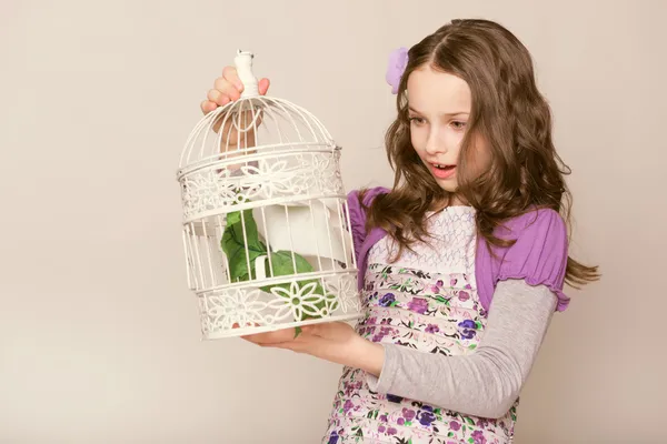Fashion little girl looks on birdcage — Stock Photo, Image