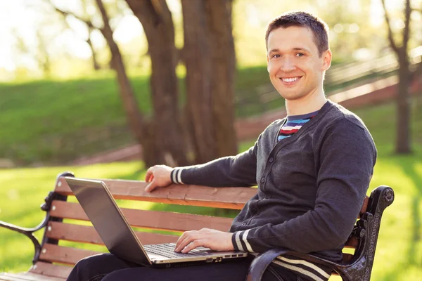 Homem com computador sentado banco no parque — Fotografia de Stock