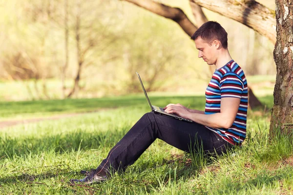 Homem trabalha com laptop em dia ensolarado no parque — Fotografia de Stock