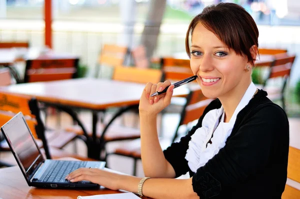 Smiley woman with laptop holding a pen in the hand Stock Photo