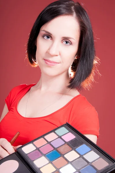 Hermosa mujer joven sosteniendo diferente maquillaje — Foto de Stock