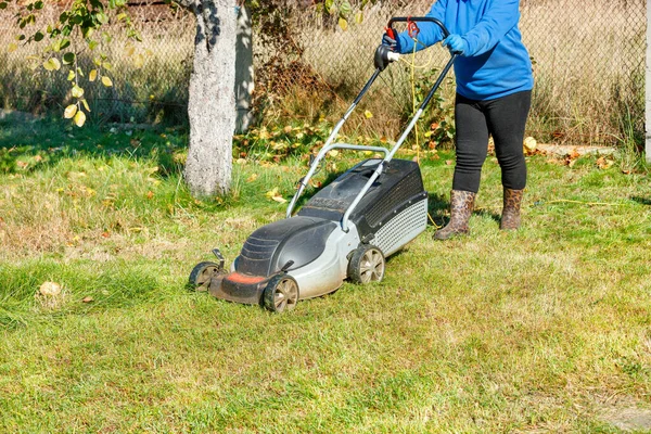 女性庭師は緑の芝生を傾向があり 明るい晴れた秋の日に裏庭に電気芝刈り機で芝生を刈る スペースのコピー — ストック写真