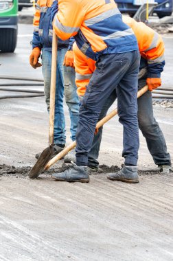 Turuncu tulumlu yol işçileri eski yol yüzeyindeki döküntüleri temizlemek için kürek kullanıyorlar..