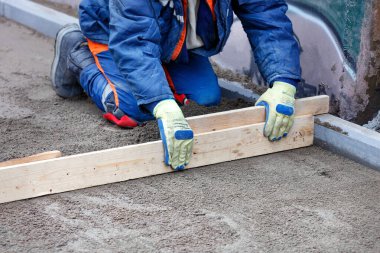 Diz çökmüş mavi işçi tulumu, gelecekte kaldırım kaplaması için ahşap bir zemine sahip kumlu bir temel oluşturur. Boşluğu kopyala.