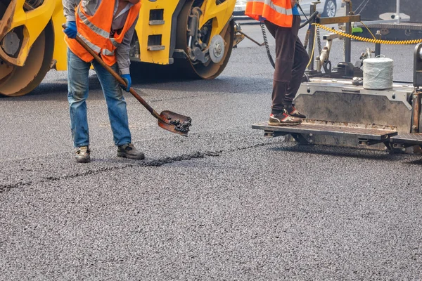 Yol işçileri, bir kürek, kaldırım ve yol silindiri ile yolun bir bölümünü onarıyor ve yola yeni bir sıcak asfalt tabakası seriyorlar. Boşluğu kopyala.