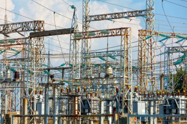 Old electrical substation with wires, metal masts and high voltage dielectric insulators against a blue cloudy sky on a sunny day.