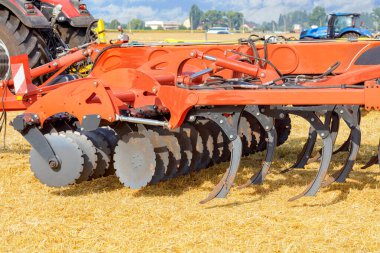 A multirow disc harrow with loosening blades is mounted on a tractor against a background of yellow stubble on a sunny warm day. Copy space. Closeup.