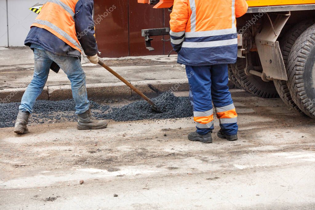 Pothole repair of the road. A team of workers levels the fresh asphalt from a truck and patches potholes on the road.