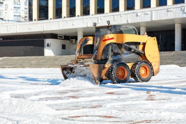 Manevra kabiliyeti olan biri açık bir kış gününde şehir meydanında kar yığınlarını temizler. Boşluğu kopyala.