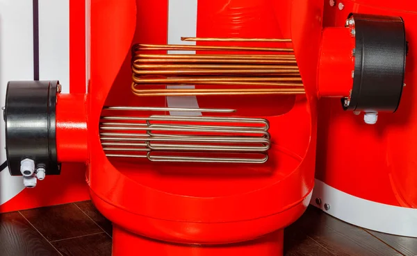 Heating elements of a powerful industrial electric boiler against the background of a red tank in a section.