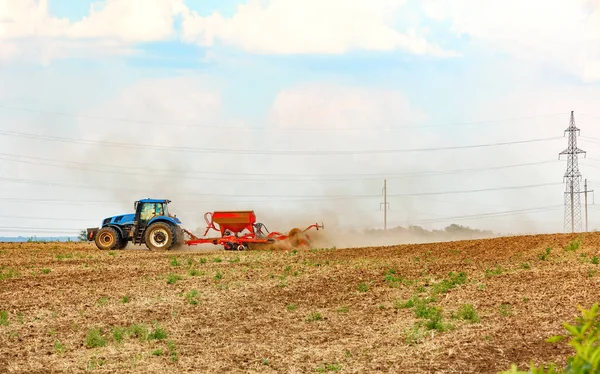 Agricultural tractor with a modern sowing machine on a freshly plowed field on a spring day. Blue tractor and red seeder on the field. Copy space.