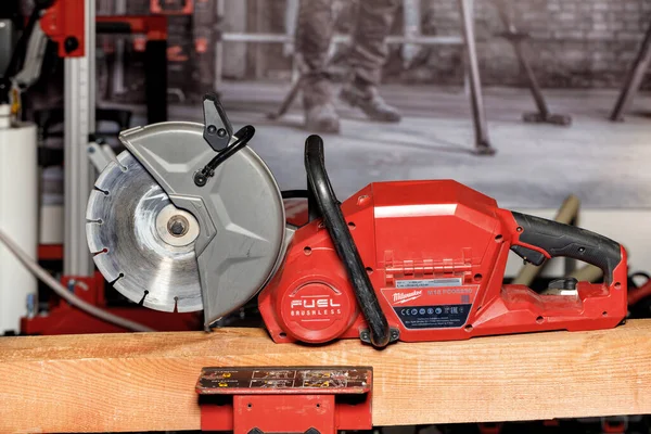 A portable red Milwaukee electric cutter with a diamond cutting wheel on a wooden beam and a blurred background. 16.2.222. Kyiv. Ukraine.