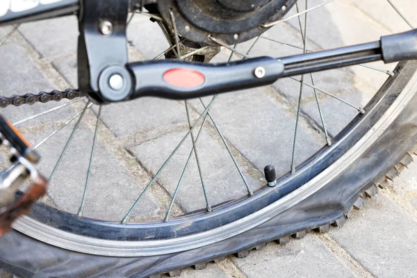 在灰色铺路板的背景上的一个被刺穿的扁平自行车轮胎 — 图库照片