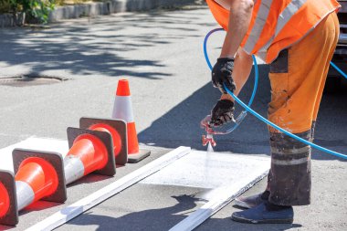 Boya spreyi kullanan bir yol işçisi tahta bir şablon kullanarak yaya geçidine beyaz yol işaretleri uygular. Boşluğu kopyala.