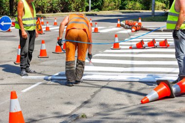 Yol işçilerinden oluşan bir ekip at arabasının çitli bir bölümünde yaya geçidi için beyaz yol işaretleri olan bir boya püskürtücü ile. Boşluğu kopyala.