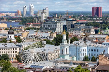 Ferris wheel in the historical center of Kyiv, Ukraine. The bell tower of the former Greek monastery on Kontraktova Square in Kyiv against the background of the upper city landscape. 07.24.22 Kyiv. Ukraine.