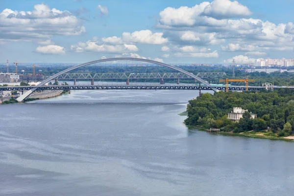 View of the new automobile cable-stayed bridge across the Dnipro River in Kyiv on a summer day against the backdrop of the urban landscape, wide water surface of the blue cloudy sky.