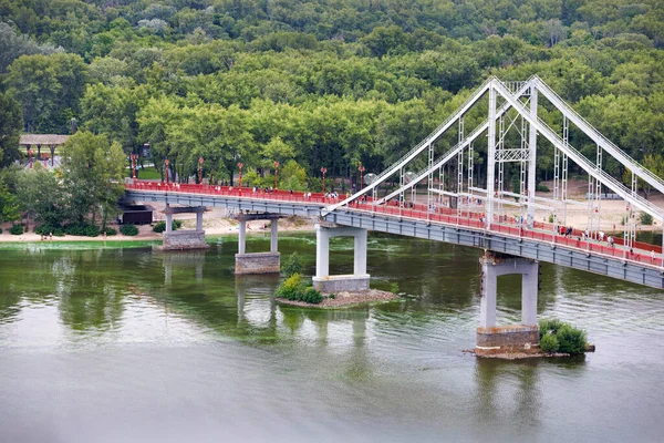 Pedestrian bridge across the Dnipro river in Kyiv on a summer day leading to a green summer recreation park.