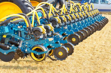 Multi row seeder with a pneumatic mechanism for even distribution and sowing of seeds against the backdrop of an agricultural field on a sunny day.