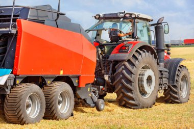 A tractor with a large red two-axle trailer for harvesting against the background of a harvested wheat field. Closeup.