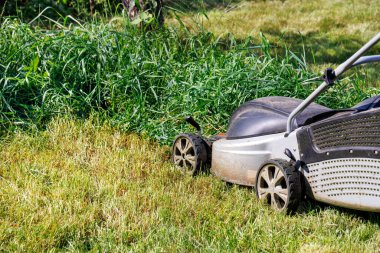 Mowing the lawn with an electric lawn mower. Fragment of an electric lawn mower and green grass. Closeup. Copy space.