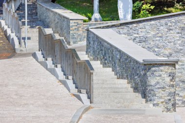 Granite steps in a modern city park with stainless steel metal railings on a sunny day against the backdrop of landscaping.