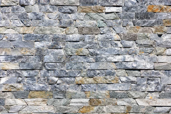Texture and background of a stone wall made of asymmetric natural gray granite tiles laid out horizontally. Texture illuminated by sunlight.