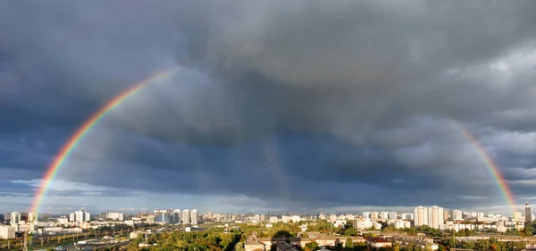 Large rainbow semicircle in the cloudy sky over the city. City landscape after the rain in a light blur.