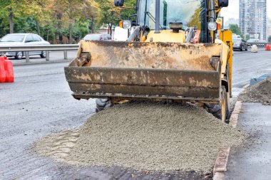 Sarı fren direksiyon yükleyicisi yol tamiri üzerine kum çakıl yükleme ve boşaltma karışımı. İnşaat ve onarım kavramı.