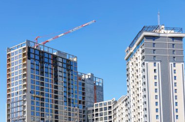 Gökyüzünün mavi arka planında bir kule vinci olan çok katlı modern bir bina inşaatı.