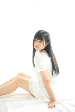 Güzel, genç Asyalı yatakta oturuyor. Sabah ışığında dinleniyor. Beyaz odalı.