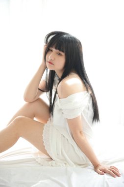 Güzel, genç Asyalı yatakta oturuyor. Sabah ışığında dinleniyor. Beyaz odalı.