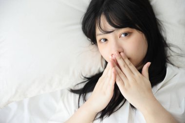 Güzel genç bir kadın sabah beyaz yatak odasında uyanıyor.