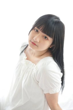 Güzel, genç Asyalı yatakta oturuyor. Sabah ışığında dinleniyor. Beyaz odalı.