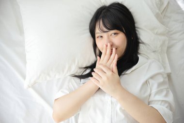 Güzel genç bir kadın sabah beyaz yatak odasında uyanıyor.