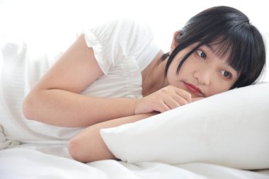 Güzel, genç Asyalı bir kadın yatakta uyuyor. Sabah güneşinde dinleniyor. Beyaz odalı.