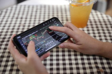 Kafede borsa alım satımı için akıllı telefon kullanan bir kadın, iş konsepti.