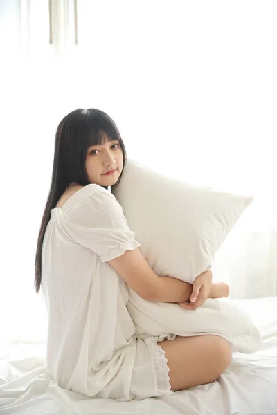 美丽的年轻亚洲人坐在床上枕着枕头 在晨光中悠闲自在 房间洁白 — 图库照片