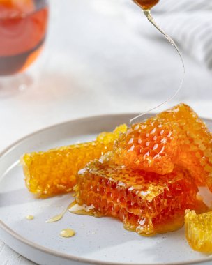 Bal tarağı bir tabakta, yakından, bal kaşığından damlayan bir damlacıktan