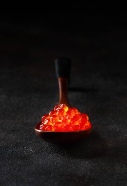 Kırmızı havyar, tahta kaşıkta, koyu bir arka planda, yakın plan.