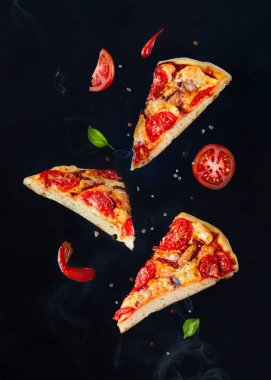 Bitkilerle, soslarla ve baharatlarla uçan pizza parçaları.