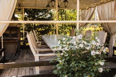 Ön planda çiçekler var. Yaz bahçesinde beyaz çardak. Bahçe mobilyası. Özel bahçede dinlenme ve dinlenme.