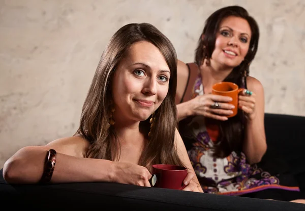 Senhoras sorridentes no sofá com canecas — Fotografia de Stock