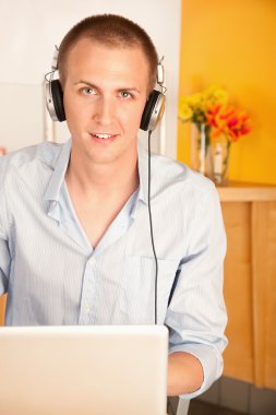 adam bir dizüstü bilgisayar üzerinde çalışan ve kulaklık takmış.