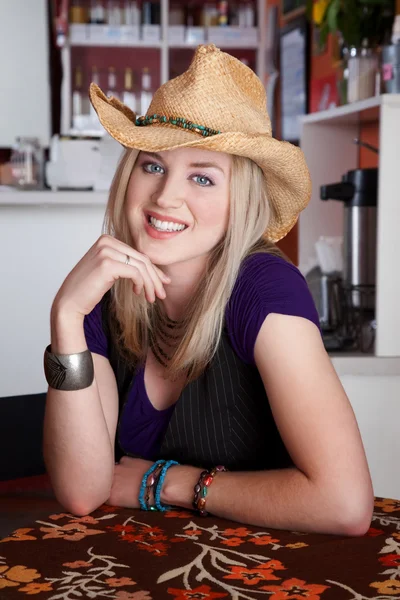 Smiling young blonde woman with cowboy hat in a cafe — Stock Photo, Image