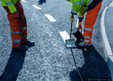 Yeni kavşak ve yol inşaatı sırasında yeni döşenmiş asfalt üzerinde termoplastik yol işareti uygulayan yol işçisi