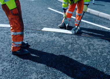 Yeni kavşak ve yol inşaatı sırasında yeni döşenmiş asfalt üzerinde termoplastik yol işareti uygulayan yol işçisi