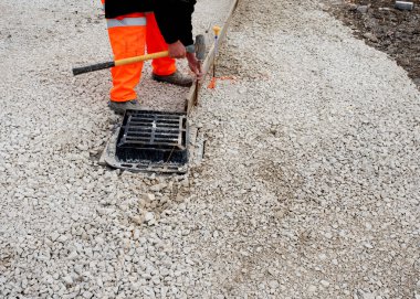 Turuncu güvenlikli bir bahçıvan. Pantolon ve yeni yol inşaatı sırasında asfalt yol yüzeyi için düz bir kenar oluşturmak için çelik çiviyle iplik hattı boyunca bir keresteyi tamir eden pantolon.